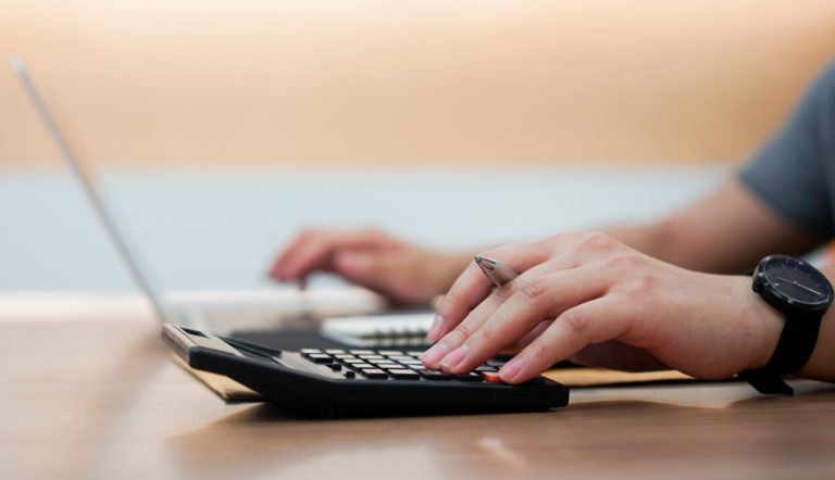 Hands using calculator and laptop